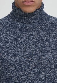 Mornarsko modra pletena turtleneck pulover z teksturiranim vzorcem, ki se ponaša z visokim ovratnikom in mehkim, debelim tkanjem.