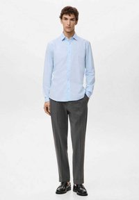 Jasnoniebieska koszula z długim rękawem i kołnierzykiem zapinanym na guziki, zestawiona z szarymi, dopasowanymi spodniami i czarnymi butami, na białym tle.