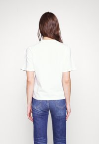 Witte katoenen t-shirt met korte mouwen en ronde hals, weergegeven vanaf de achterkant, gecombineerd met blauwe denim jeans met subtiele vervaging.
