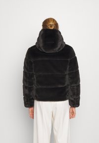 Svart fake pälsjacka med huva, i en fluffig design med horisontella sömmar. Bakifrån syns en kortad längd och en mjuk textur.