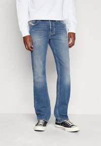 Jeans de mezclilla azul con un diseño de pierna recta, ligero desgaste y costuras en contraste. Combinados con zapatillas de lona negras.