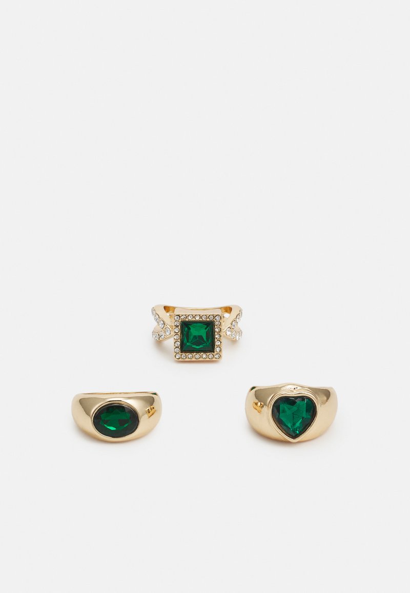 Três anéis de ouro com gemas verdes: um quadrado com realces claros, dois arredondados com formas ovais e de coração, todos com texturas lisas.