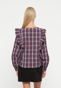 Rood en blauw geruite blouse met rimpelige schouderdetails, lange mouwen en een vierkante halslijn. De stof heeft een gladde textuur.