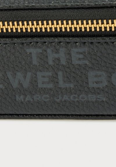 Μαύρο πορτοφόλι από δέρμα με υφή και χρυστό φερμουάρ. Διαθέτει ανάγλυφη επωνυμία: «THE JEWEL BOX» και «MARC JACOBS» με διακριτικό φινίρισμα.