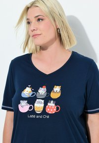 Granatowa koszulka z dekoltem w serek, ozdobiona kolorową grafiką kotów w kubkach, z napisem "Latté i Chill". Białe akcenty na rękawach.