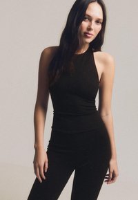 Czarny, bezrękawnik w fasonie halter z dopasowanym krojem. Materiał ma subtelny blask. Gładka tekstura. W zestawie z dopasowanymi spodniami.