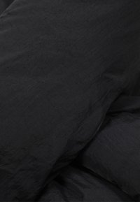 Sort sengetøjssæt med en krøllet tekstur, der har blødt stof og en glat overflade, lagdelt med en let rynket udseende.