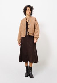 Veste courte en tissu texturé marron avec des boutons noirs, associée à une robe marron mi-longue et des bottines noires.