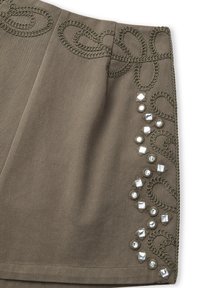 Falda de tela verde oliva con un patrón decorativo de puntada de cadena en la cintura y acentos de tachuelas plateadas a lo largo del dobladillo. Textura suave.