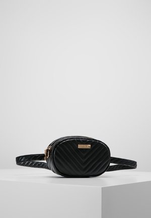 Petit sac ceinture en cuir noir matelassé avec fermeture éclair dorée et plaque métallique de marque à l'avant, présenté sur un socle blanc sur fond gris.