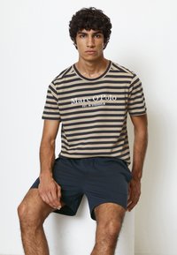 Randig kortärmad t-shirt i beige och mörkblå, med rundad hals och vit texttryck. Matchas med mörka shorts.