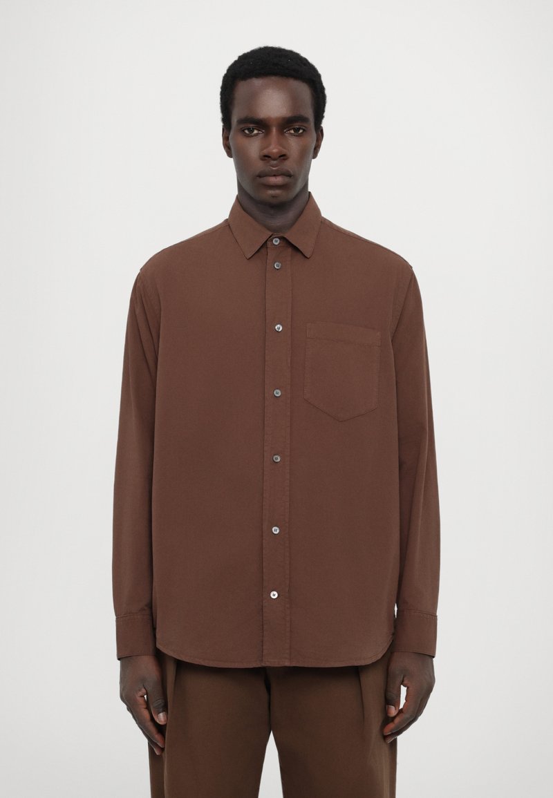 Chemise brune à manches longues, à boutons, avec col, poche poitrine unique, texture lisse et ourlet arrondi, associée à un pantalon assorti.