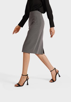 Donna che cammina indossando una maglia nera a maniche lunghe, una gonna a matita grigia fino al ginocchio e sandali neri con tacco alto e cinturini alla caviglia.