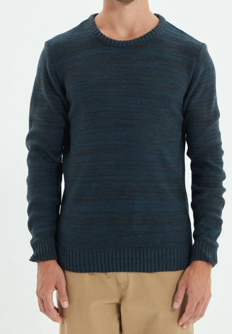 Pull bleu foncé rayé avec un col rond, un tricot texturé et des poignets et ourlet côtelés. Associé à un pantalon beige clair pour le contraste.