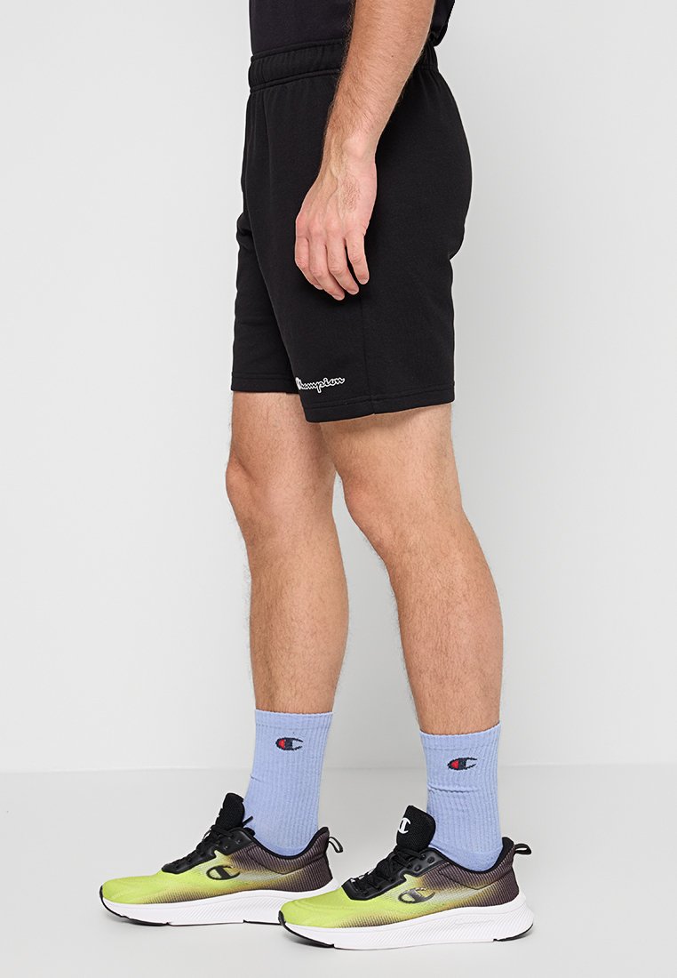 Pantalones cortos atléticos negros con una cintura elástica, combinados con calcetas de color azul claro y zapatillas con degradado. Los pantalones cortos cuentan con un pequeño detalle de logo.