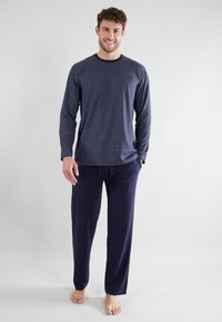 Navy striped long-sleeve shirt with rounded neckline and loose fit, paired with soft navy drawstring pants in a relaxed style.