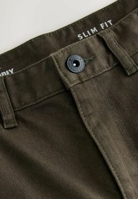 Slim fit püksid oliivrohelisest puuvillakangast. Omavad musta nööbi sulgemist, toon-toonis õmblusi ning sileda tekstuuri.