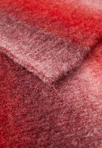 Tejido de lana suave y texturizado con una esquina doblada, que muestra un degradado de tonos rojos a rosas y una superficie peluda.