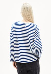 Langärmliges Shirt in Weiß mit blauen horizontalen Streifen, mit einem gerundeten Halsausschnitt und überschnittenen Schultern. Weicher Baumwollstoff mit einem lockeren Schnitt.