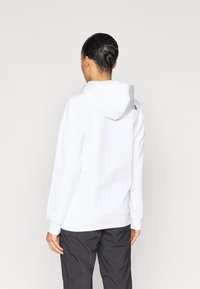 Λευκό φούτερ με κουκούλα, ριμπ μανσέτες και ρίγα στη μέση. Διαθέτει μικρό μαύρο λογότυπο στην πλάτη. Το ύφασμα φαίνεται απαλό και με υφή.