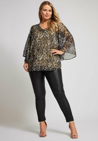 Top trasparente con stampa leopardata, scollatura a V, maniche larghe, abbinato a pantaloni neri aderenti e sandali con tacco dorati. Design morbido e fluido.