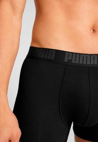 Black cotton boxer briefs with a wide black waistband featuring embossed "PUMA" logo. Smooth texture, fitted design, and standard length.