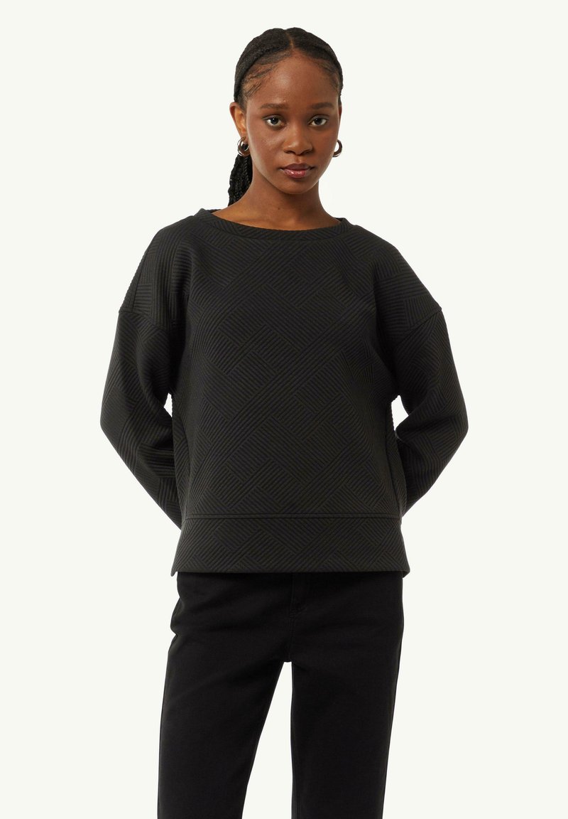 Schwarzer Pullover mit strukturiertem geometrischem Muster, weitem Ausschnitt und überschnittenen Schultern, kombiniert mit schwarzen Hosen. Glatte Stoffoberfläche.