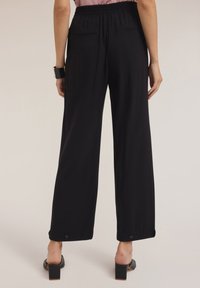 Zwarte wijde broek met een elastische tailleband, twee achterzakken en knoopaccenten aan de zoom, gecombineerd met hakken.