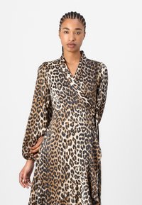Leopardprint omslagskjole med lange ærmer, lavet af glat stof. Har en dyb V-halsudskæring og en båndlukning i taljen.