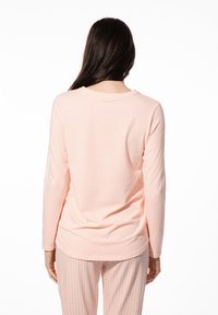Lange mouwen lichtroze shirt van zacht materiaal, met een ronde hals en een losse pasvorm, van achteren weergegeven met een patroonbroek.