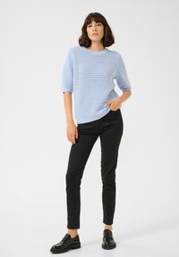 Un pull en tricot bleu clair à manches courtes, avec un design texturé, assorti à un pantalon slim noir et des mocassins noirs. Look simple et moderne.