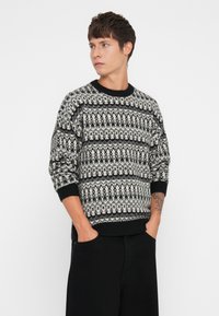 Πλεκτή ζακέτα με μαύρο και άσπρο σχέδιο και γεωμετρικά σχέδια. Στρογγυλή λαιμόκοψη, χαλαρή εφαρμογή και ριχτές μανσέτες και στρίφωμα.