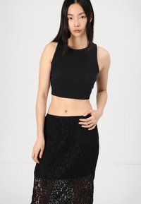 Un top scurt negru cu dungi, cu un guler rotund, asociat cu o fustă neagră din dantelă, cu modele florale și o secțiune inferioară transparentă.