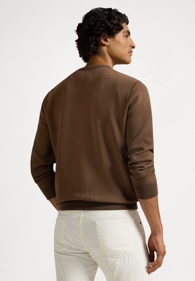 Brązowy dzianinowy sweter z okrągłym dekoltem i ściągaczami na rękawach, zestawiony z jasnymi spodniami dżinsowymi. Materiał wygląda na miękki i strukturalny.