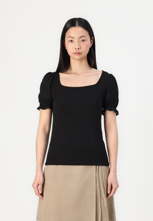 Top negro de canalé con escote cuadrado y mangas acampanadas de encaje. Diseño ajustado con una textura suave, combinado con una falda beige.
