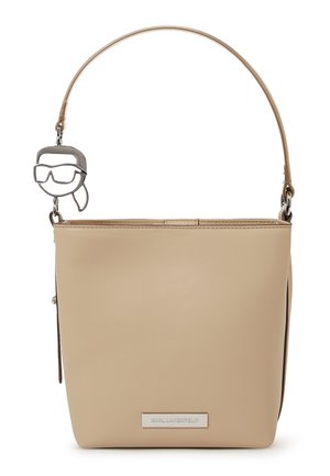 Bež ročna torbica iz sintetičnega usnja s tankim ramenskim trakom in srebrnim obeskom v obliki abstraktnega obraza z očali.