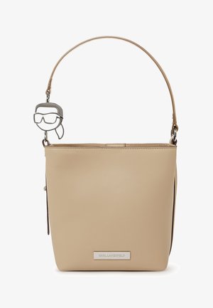 Beige synthetische Lederhandtasche mit einem dünnen Schulterriemen und einem silbernen Anhänger, der ein abstraktes Gesicht mit Brille zeigt.