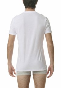 Biała bawełniana koszulka z krótkim rękawem, widoczna z tyłu. Wyraźny bezszwowy dekolt i luźny krój. Szare szorty widoczne w talii.