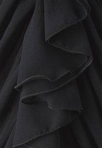 Tela negra con volantes en capas, con una textura suave y bordes cosidos contrastantes, creando profundidad visual y movimiento.