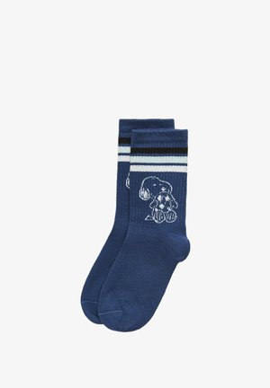 Chaussettes montantes bleues avec des rayures blanches et noires près du bord, représentant un chien de dessin animé blanc tenant une balle tachetée sur chaque chaussette.