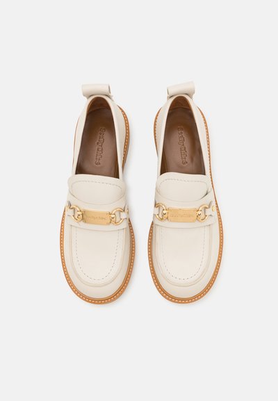 Pantofi loafers din piele de culoare albă cu un accent de lanț auriu și o talpă din cauciuc maroniu deschis. Prezintă detalii cusute și o textură netedă.