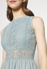 Ljusblå klänning i spets med cirkulära broderidetaljer. Har en figursydd överdel och en flödande kjol, är ärmlös.