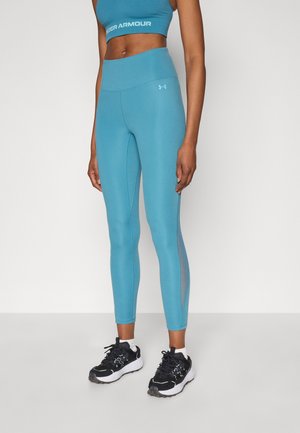 Leggings bleu clair taille haute avec panneaux latéraux texturés, fabriqués en matériau extensible. Portés avec des chaussures de sport noires.
