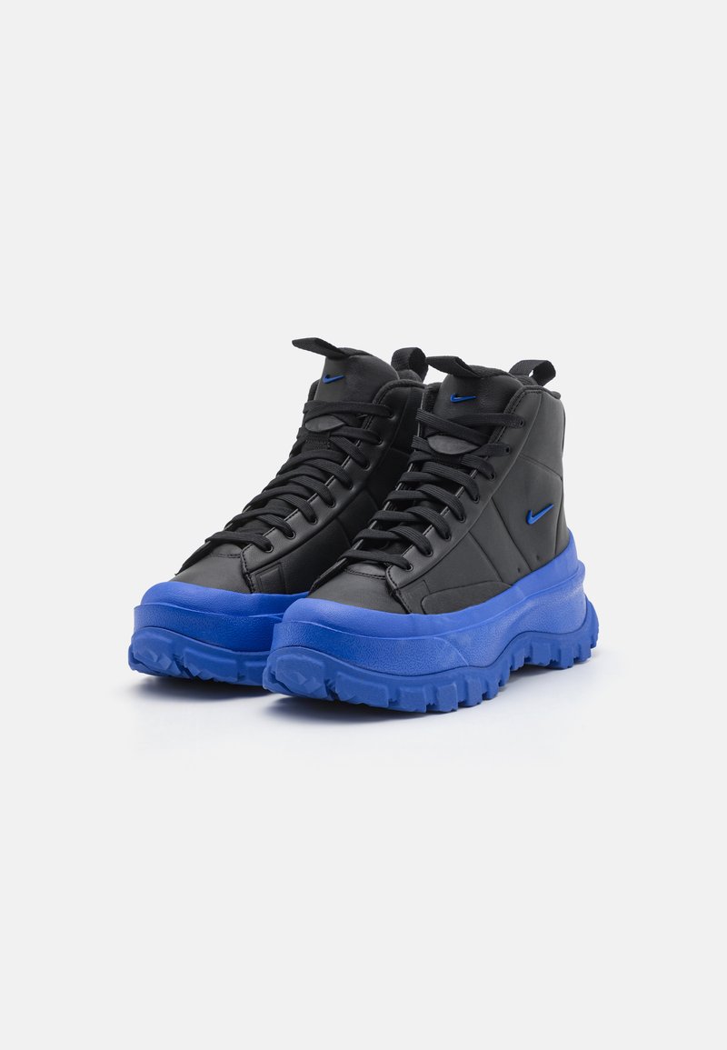 Zapatillas de deporte negras de caña alta con un upper de cuero texturizado y suela de goma azul en contraste. Cuenta con un sistema de cordones prominente y un acento de logo.