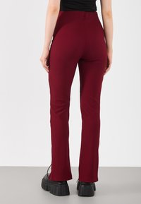 Maroon ribbed pants with a high waist, flared legs, and zip accents at the ankles, made from stretchy material.