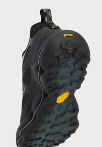 Čierne športové topánky s textúrovanou gumovou podrážkou, na ktorej je žlté logo Vibram. Zvršok má štíhly dizajn s vzorovanou látkou.