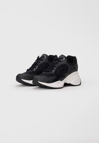 Black sneakers with textured fabric, a smooth black accent on the sides, white cushioned sole, and logo detail on the outer side.