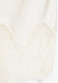 Tissu blanc soyeux avec une délicate bordure en dentelle florale présentant des bords festonnés et des motifs complexes.