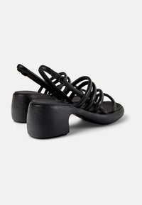 Black heeled sandals with multiple thin straps and a block heel. Textured material creates a subtle sheen. Adjustable buckle at the heel.