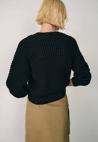 Maglione nero a maglia con texture a coste, scollatura rotonda e spalle abbassate, abbinato a una gonna beige chiaro. Vista posteriore mostrata.